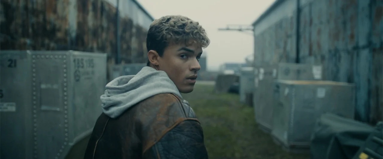 My Fault: London (2025) movie still: medium — A fenced-in industrial loading dock is filled with gray metal shipping containers and containers. A…