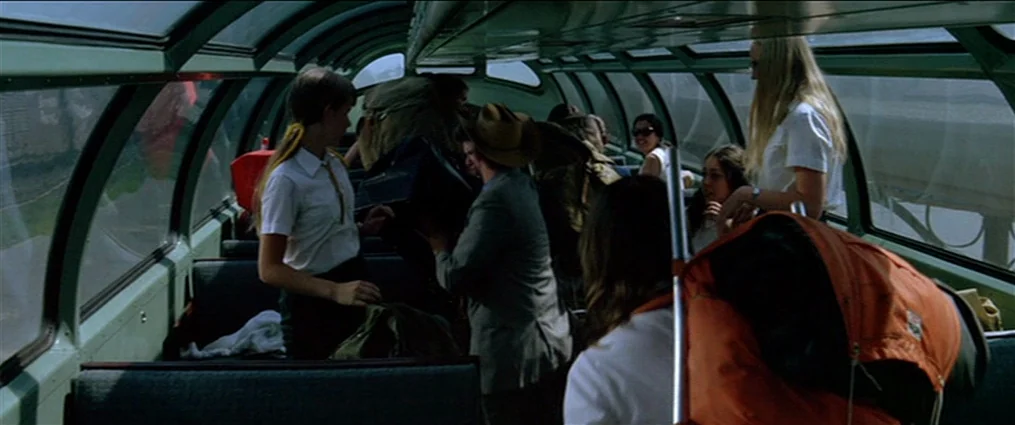 The Getaway (1972) movie still: medium — An observation car on a train features curved glass ceilings and green metal frames. Passengers manage…