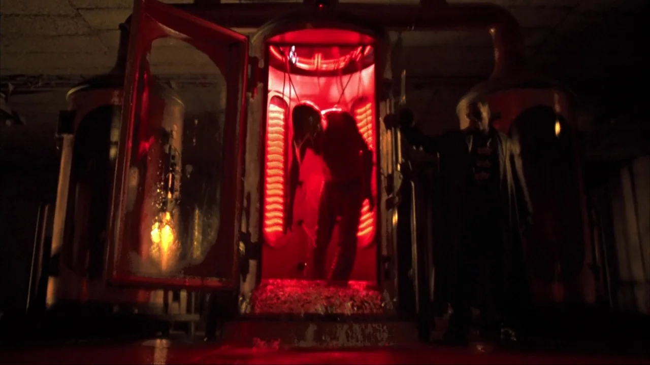 Blade II (2002) movie still: medium — A dark subterranean chamber contains large industrial metallic cylinders lit by an intense crimson glow. A man…