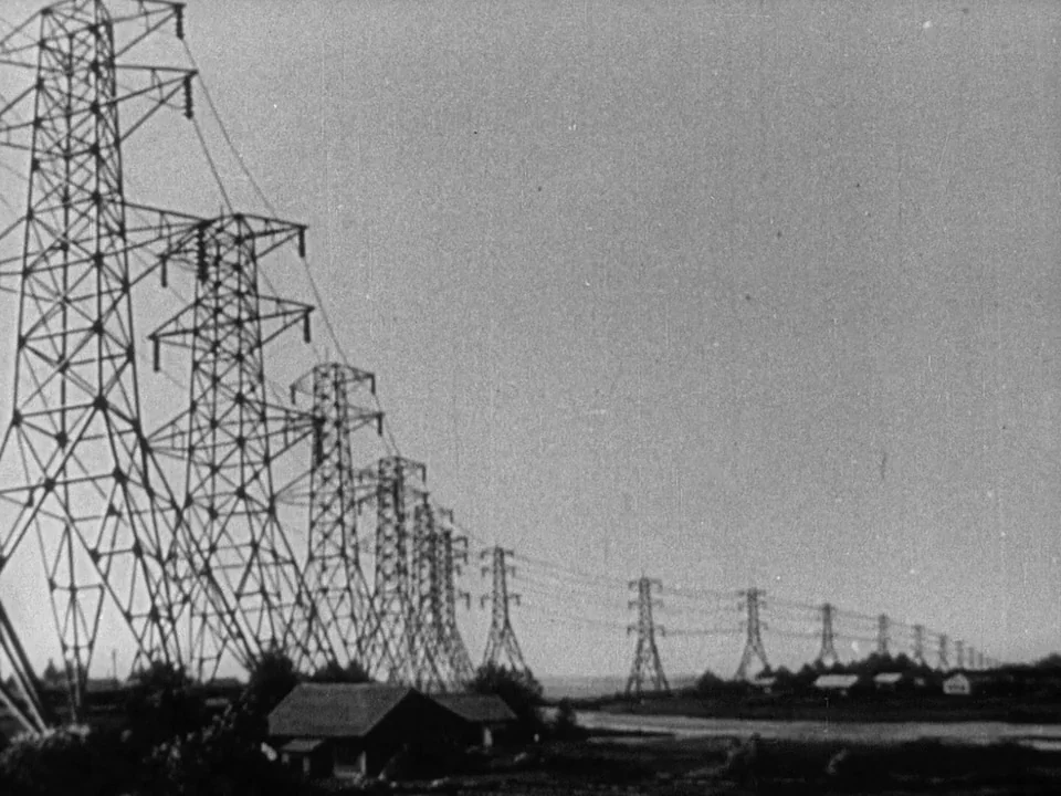 Godzilla (1954) (1954) movie still: establishing — A long row of metal electrical pylons recedes into the distance across a field. Small wooden…