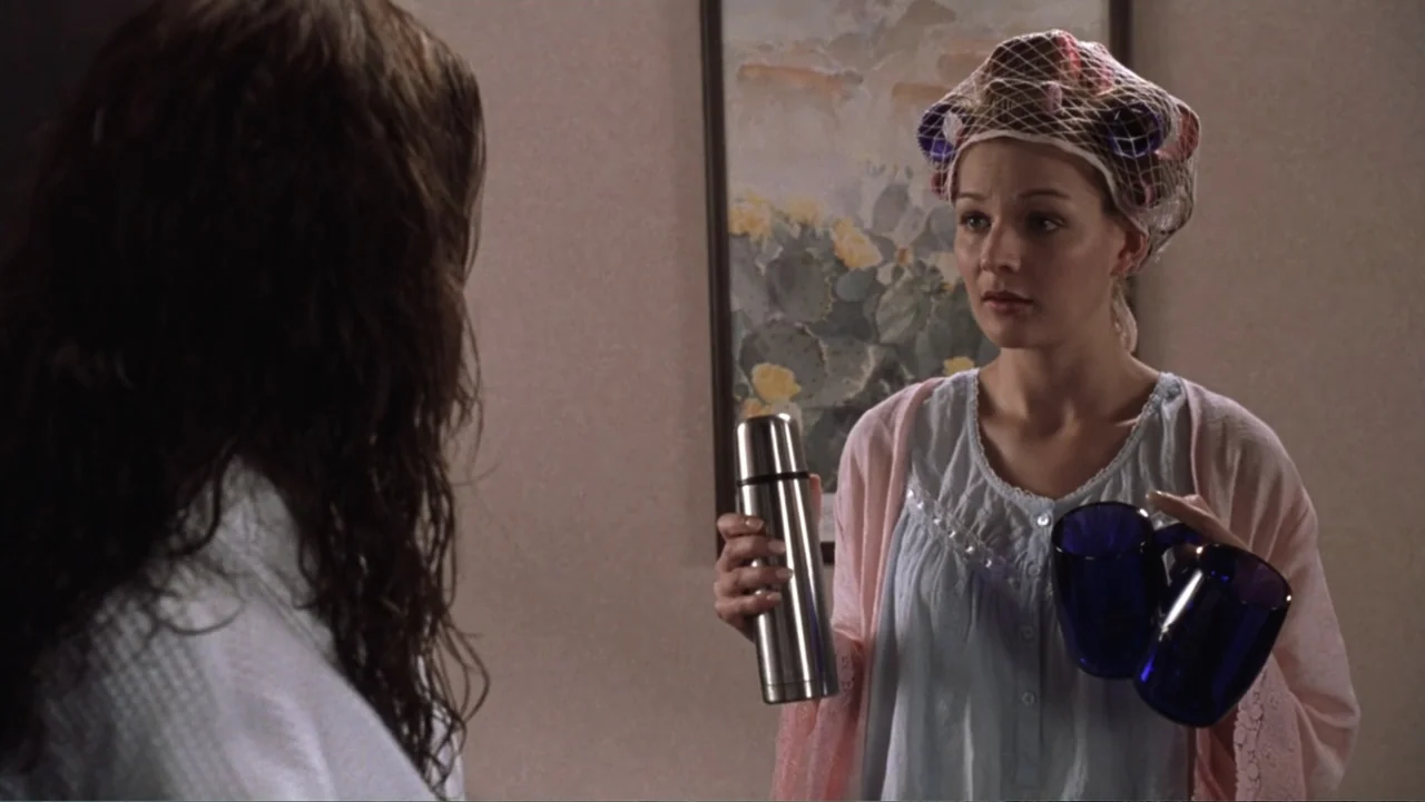 Miss Congeniality (2000) movie still: medium — A motel room with beige walls and a framed cactus print painting. A woman in curlers stands holding a…