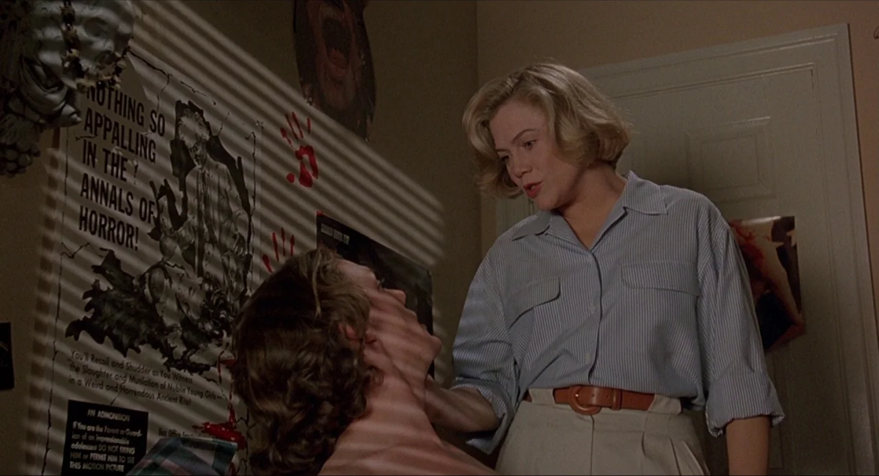 Serial Mom (1994) movie still: medium — A residential room features a vintage horror movie poster taped to the wall. A woman in a striped shirt…
