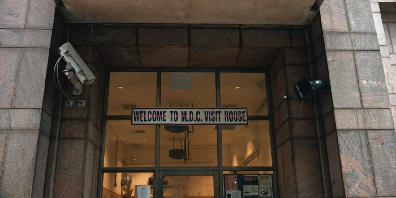 Equal Standard (2021) movie still: wide — A stone-clad entranceway features a glass door with a sign reading Welcome to M.D.C. Visit House. Security…