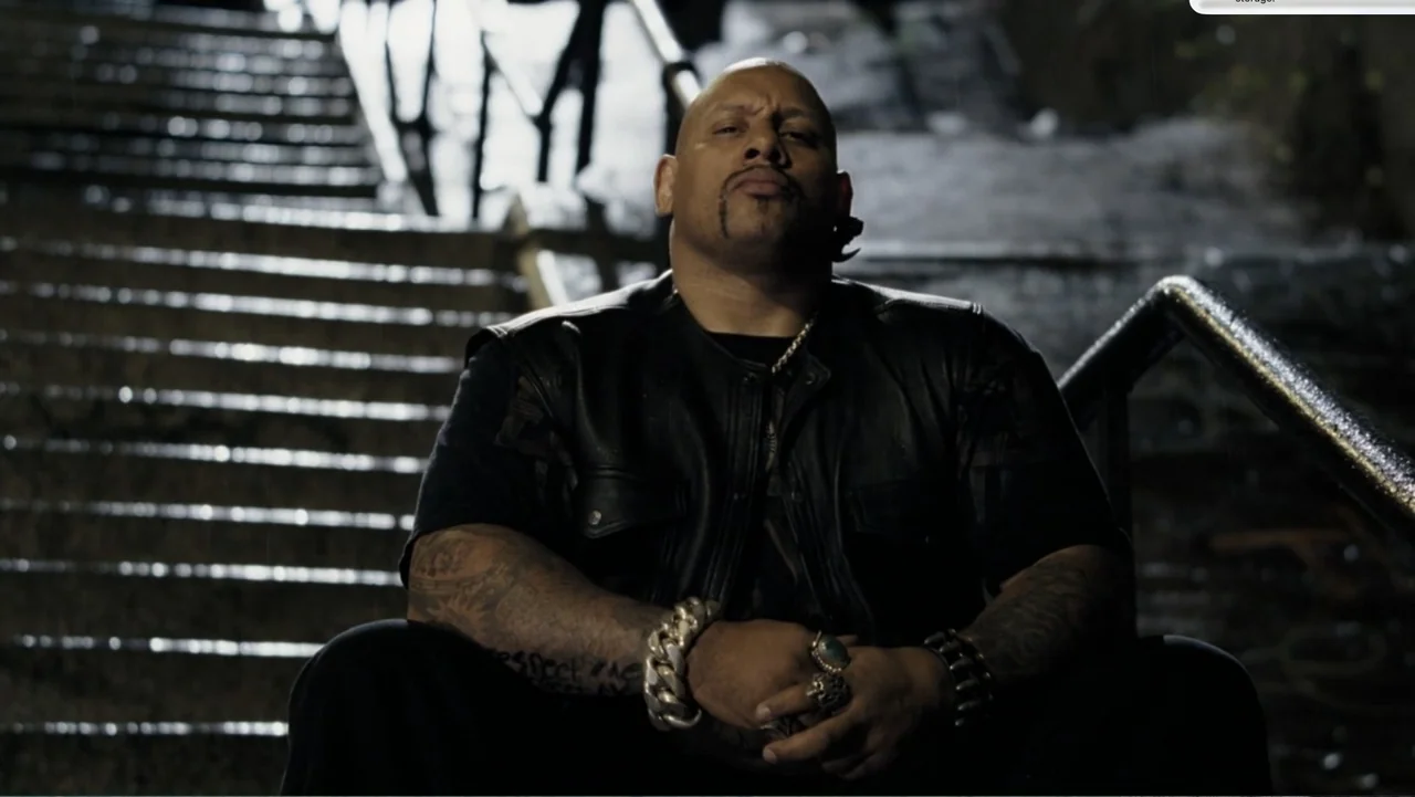 Fighting (2009) movie still: medium — A man sits on concrete stairs at night under harsh lighting conditions. He has his hands clasped and is facing…