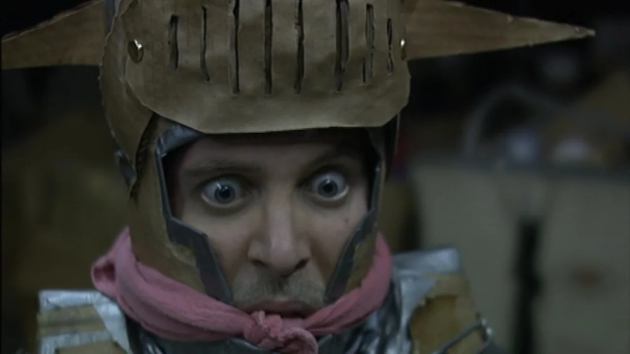 Murder Party movie still: closeup — A man wearing a makeshift knight's helmet made of cardboard and tape. The man stares directly into the camera…