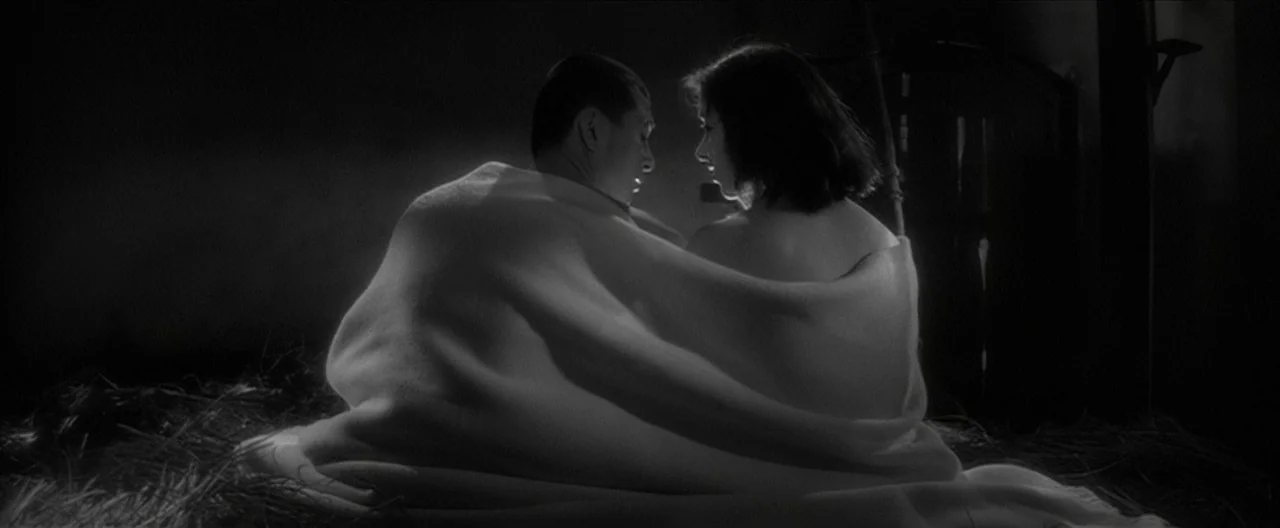 Story of a Prostitute (1965) movie still: medium — Two figures are wrapped in a large blanket while sitting upon dried hay. The scene is illuminated…
