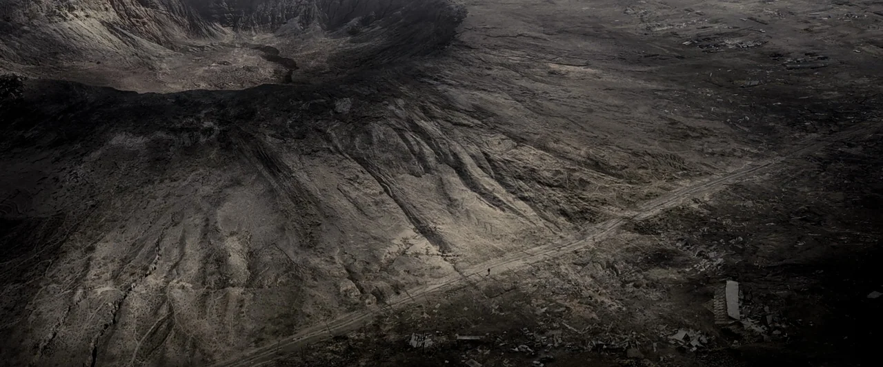 The Book of Eli (2010) movie still: establishing — A vast, barren volcanic crater sits beneath a wide, desolate landscape of dry earth. A solitary,…