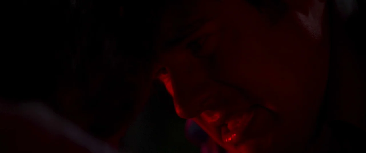 Summer of 84 (2018) movie still: closeup — A dark, underexposed interior space is shrouded in near-total shadow. A man's face is partially lit by a…