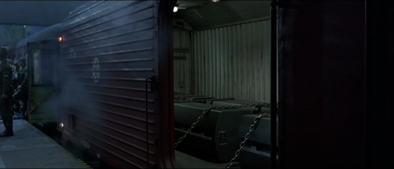 The Peacemaker (1997) movie still: wide — A dark train station platform with a corrugated red cargo carriage parked alongside it. The open door of…