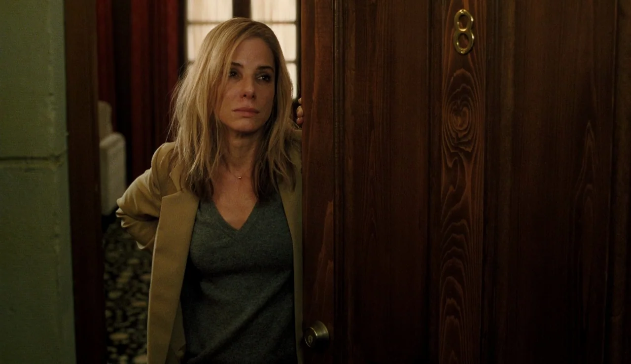 Our Brand is Crisis (2015) movie still: medium — A woman stands behind a wooden hotel door marked with a gold number eight. She looks out from the…