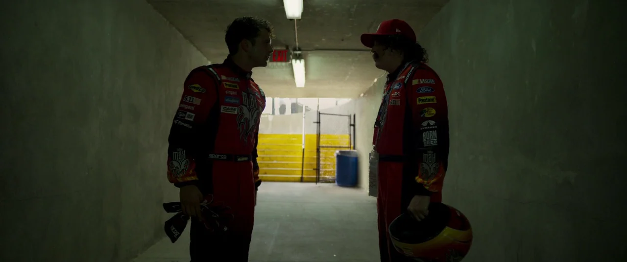 Logan Lucky (2017) movie still: fullbody — A dark concrete tunnel illuminated by overhead fluorescent lights leads toward a bright exit. Two male…