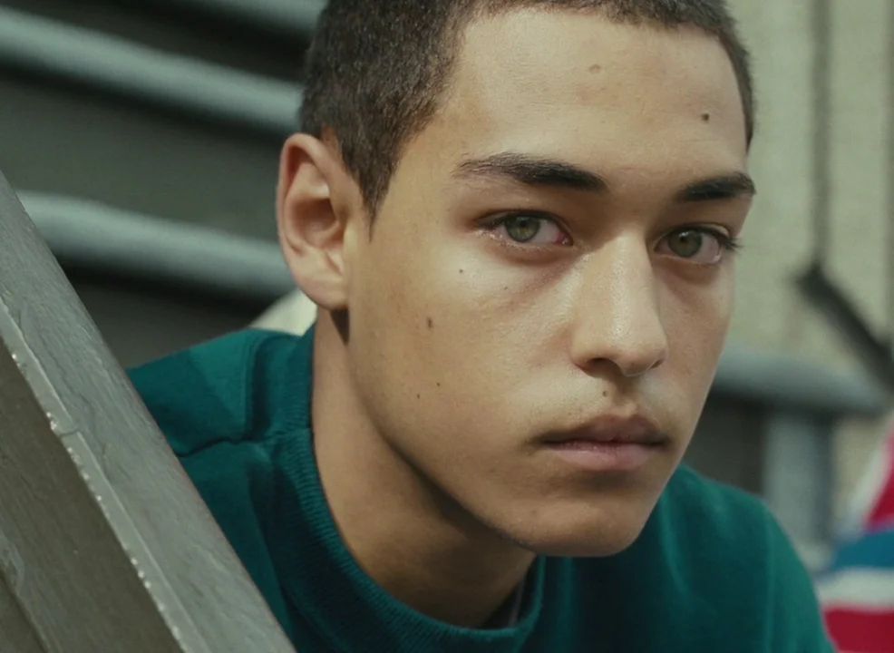 Laurence Anyways (2012) movie still: closeup — A close-up shot of a young man against an outdoor staircase railing. The subject looks forward with a…