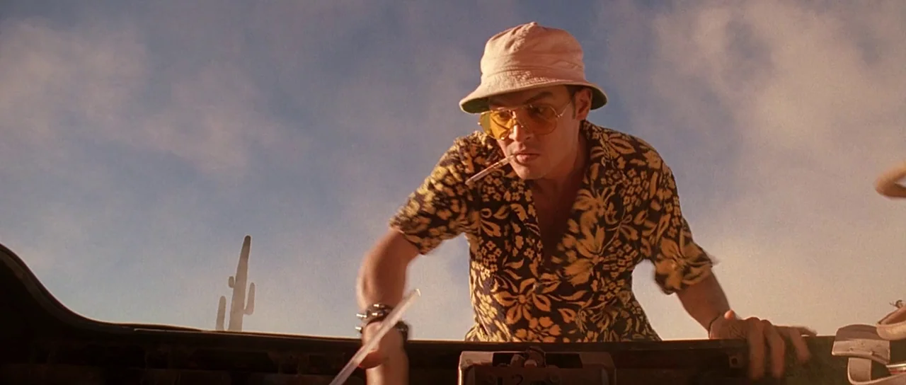 Fear and Loathing In Las Vegas (1998) movie still: medium — A man stands in an arid landscape with a cactus visible against the sky. He reaches into…