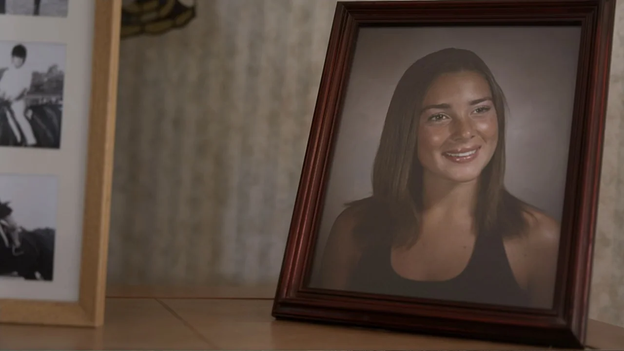 Predators (2010) movie still: closeup — A framed portrait of a young woman sits on a table surface. The portrait features a teen girl smiling,…