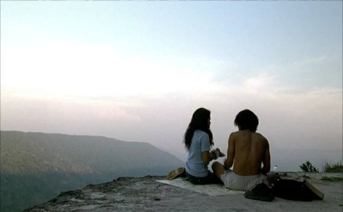Blissfully Yours (2002) movie still: wide — A man and a woman sit on a rocky cliff overlooking a vast mountain range. They are positioned on a flat…