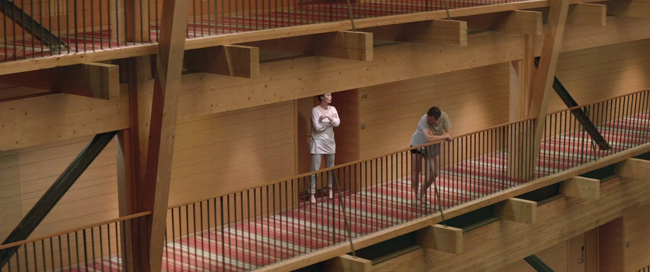 Force Majeure (2014) movie still: wide — A modern building interior features multi-level wooden balconies with thin metal railings. A man and a…