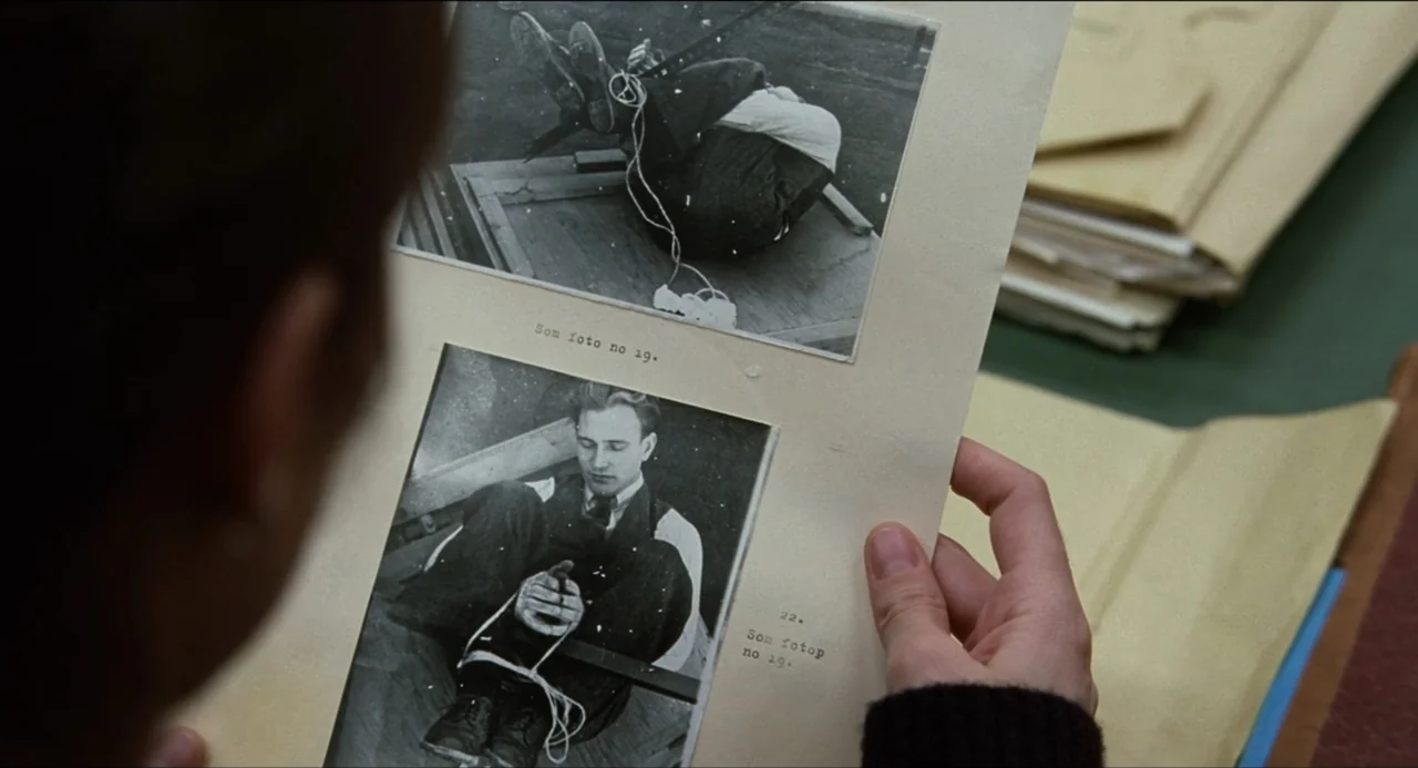 Sentimental Value (2025) movie still: closeup — A person holds a document containing two printed photographs of a bound man. The paper sits in front…