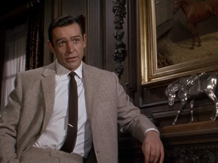 Marnie (1964) movie still: medium — A wood-paneled room features a mantelpiece with a silver horse statuette and framed artwork. A man in a tweed…