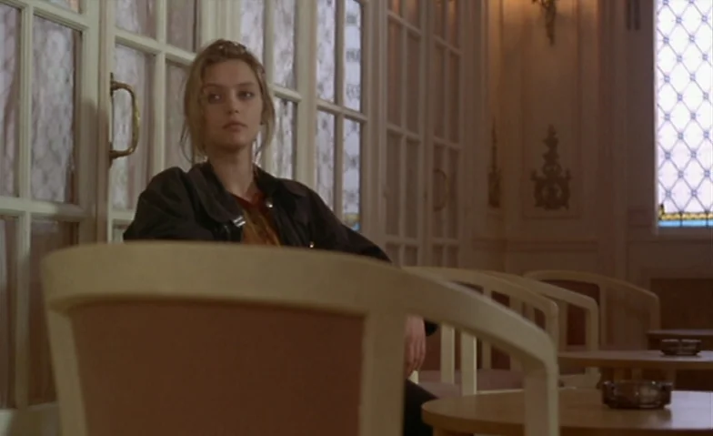 I Can’t Sleep (1994) movie still: medium — A quiet lobby area features light-colored wooden chairs and glass panel partitions. A young woman sits in…