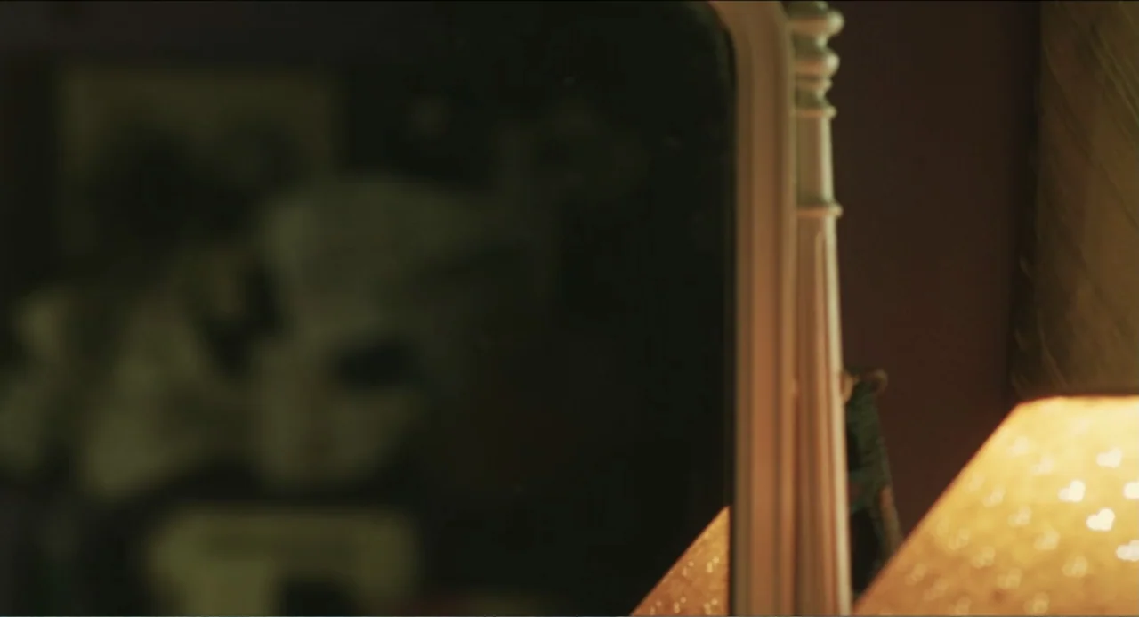 Haunter (2013) movie still: closeup — A close-up shot focuses on the reflective edge of a wooden mirror frame. A soft lamp glow illuminates the…