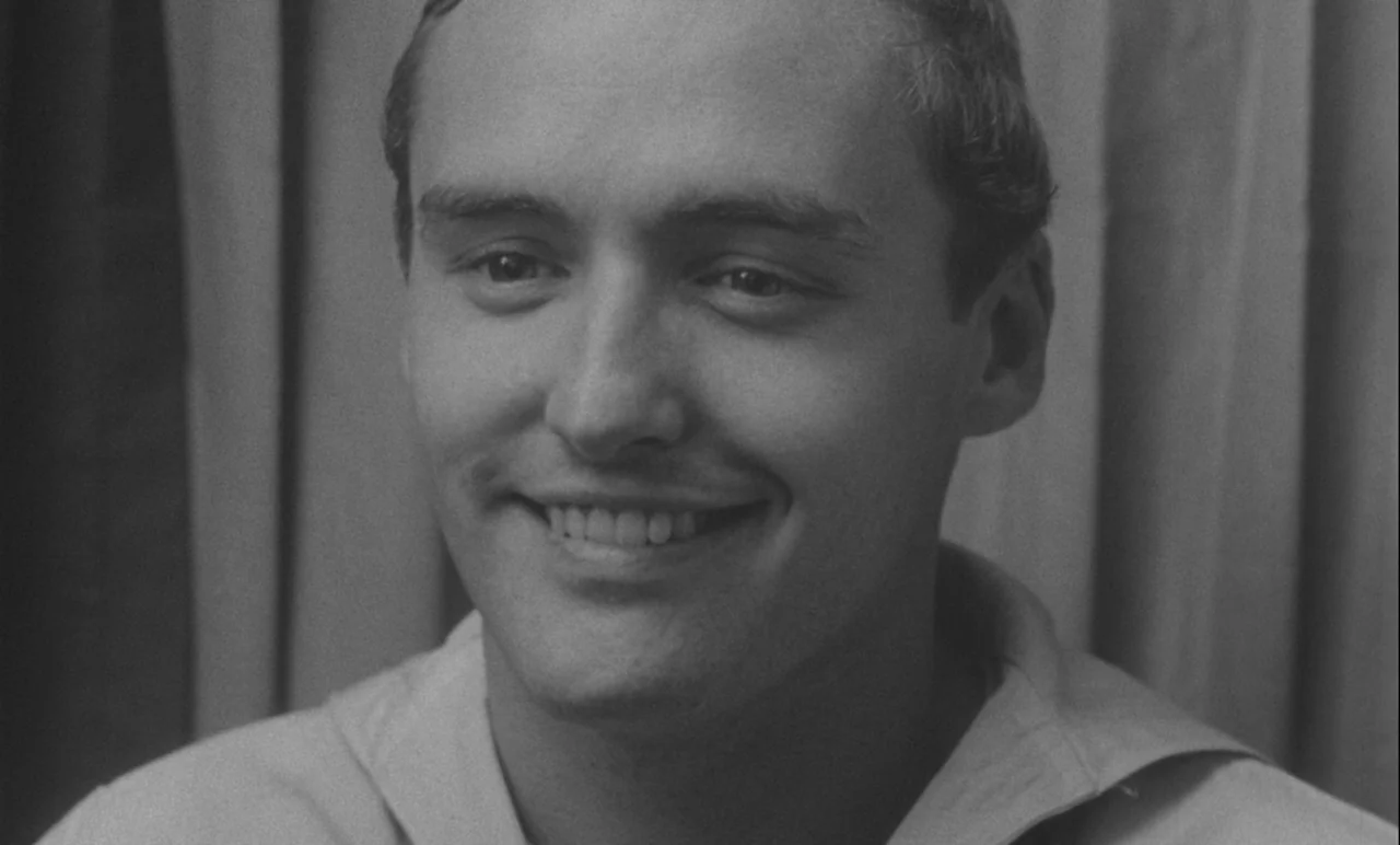 Night Tide (1961) movie still: closeup — A close-up shot of a man's face against a simple draped background. The subject smiles broadly while…