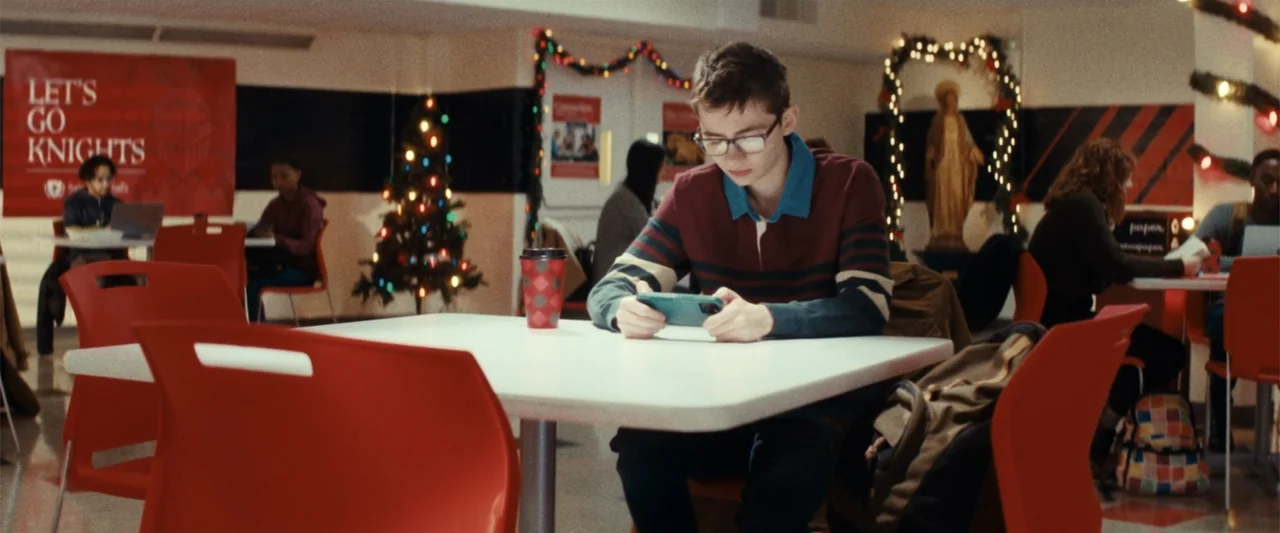 Terrifier 3 (2024) movie still: medium — A school cafeteria decorated for Christmas with festive garlands and a small tree. A teenage boy sits at a…