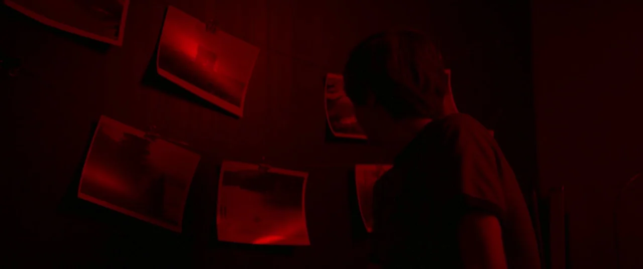 Summer of 84 (2018) movie still: medium — A darkroom features multiple photographic prints suspended from a horizontal wire against a wall. A young…