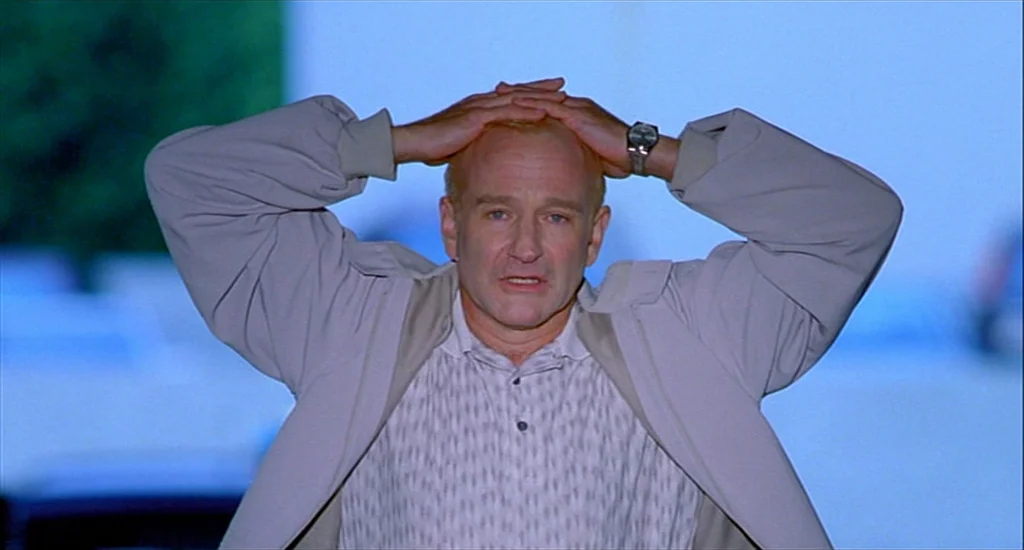 One Hour Photo (2002) movie still: medium — A man stands outdoors at night in an open space under blue-toned lighting. He places both hands on his…