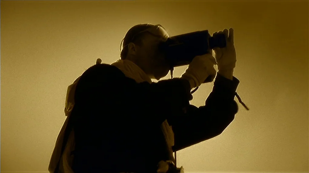 The State of Things (1982) movie still: medium — A figure stands in a featureless yellow-toned environment against a solid backlit background. The…