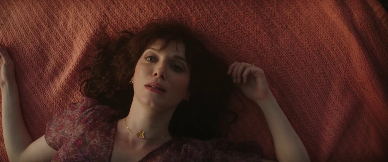 God’s Pocket (2014) movie still: closeup — A woman lies on a textured reddish-orange fabric covering the ground. She looks directly upward with an…