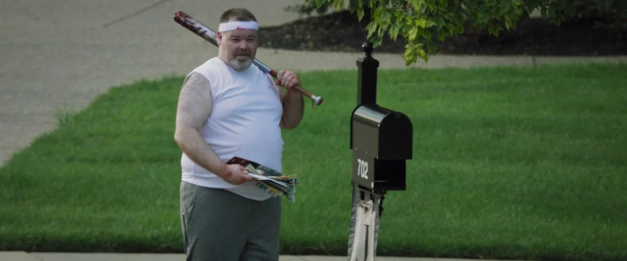 Mom and Dad (2017) movie still: medium — A man stands on a suburban lawn beside a black mailbox labeled 702. He holds a baseball bat over his…