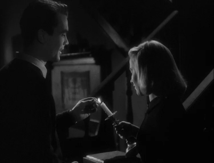 Music in Darkness (1948) movie still: medium — A dimly lit staircase interior features a staircase railing in the background. A man lights a candle…
