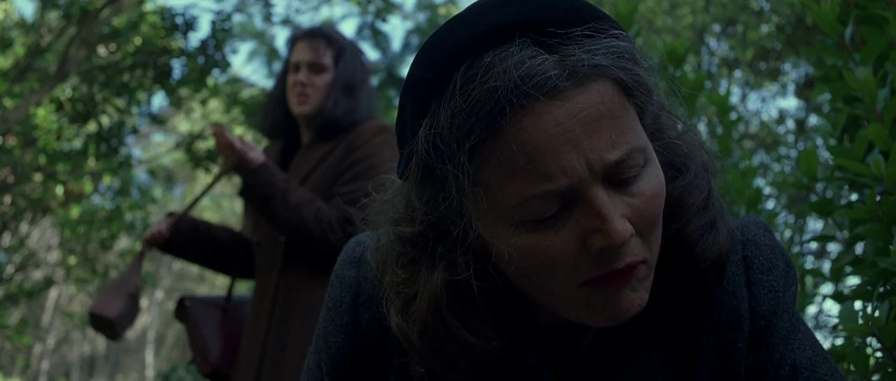 Heavenly Creatures (1994) movie still: medium — Two women stand in a dense forest during the daytime. One woman is in the foreground looking…