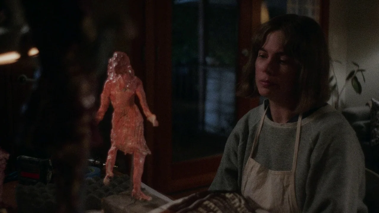 Showing Up (2022) movie still: medium — An artist works in a dimly lit studio space at night. A small red clay figure stands on a table before her.