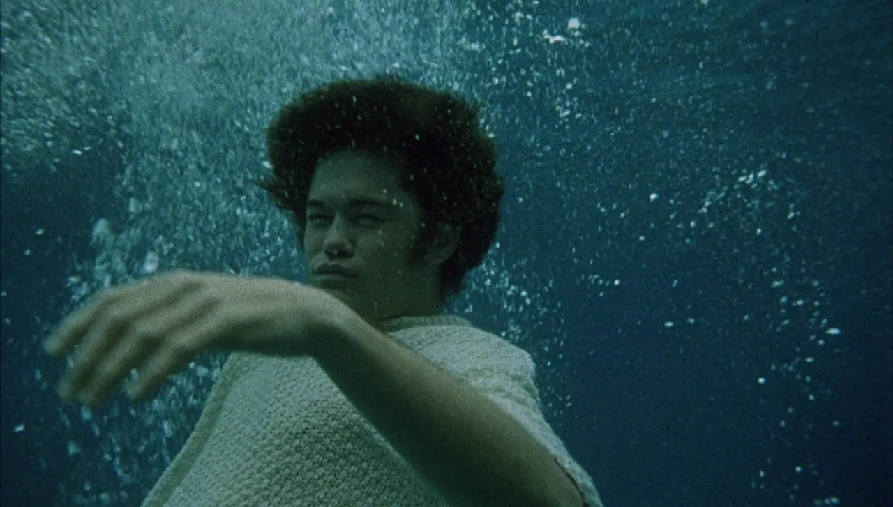 Head (1968) movie still: medium — A person is submerged deep underwater in a dark, deep blue environment. Bubbles rise past the individual as they…