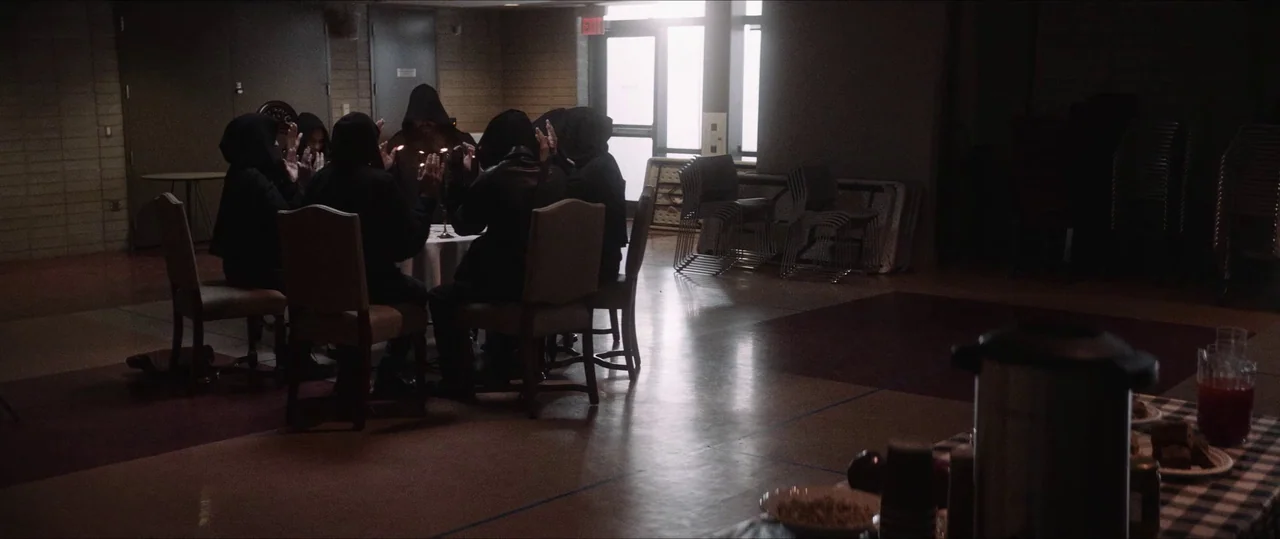 Anything For Jackson (2020) movie still: wide — A spacious community hall with tan walls and linoleum flooring contains a central table. Seven…