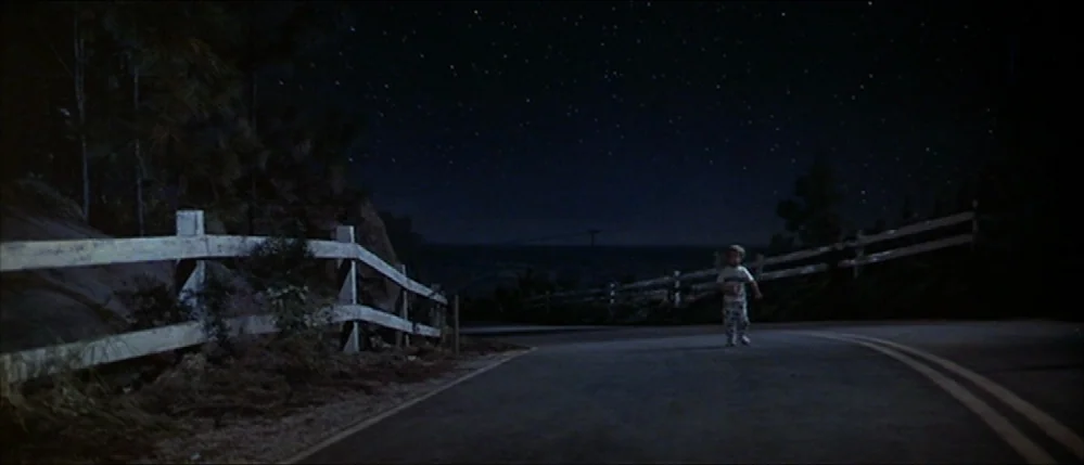 Close Encounters Of The Third Kind (1977) movie still: wide — A rural asphalt road curves through a landscape under a clear, starry night sky. A…