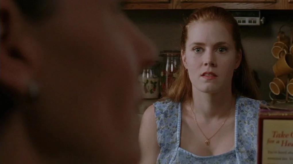 Junebug (2005) movie still: medium — A woman stands in a home cooking area with cabinets and mugs visible. She looks directly toward a person…