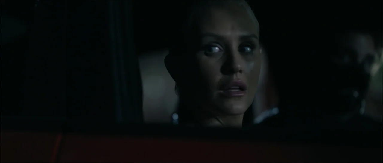 Crescent City (2024) movie still: closeup — A dark vehicle interior with very low ambient light levels. A blonde woman sits in the driver seat…