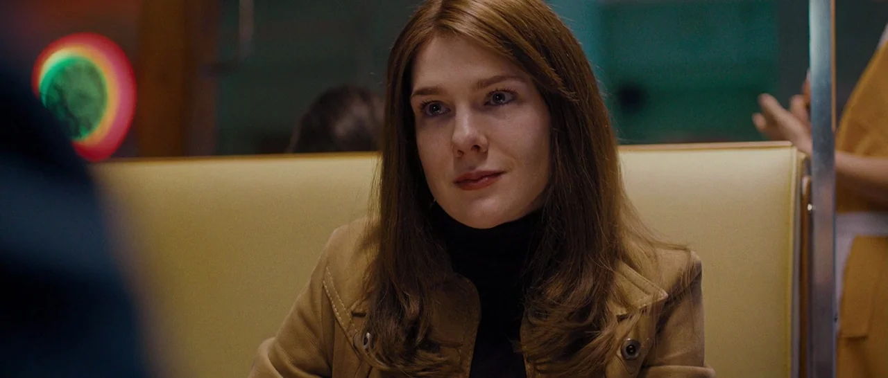 Pawn Sacrifice (2014) movie still: medium — A woman sits inside a diner booth with yellow upholstery and teal walls. She looks toward the camera…