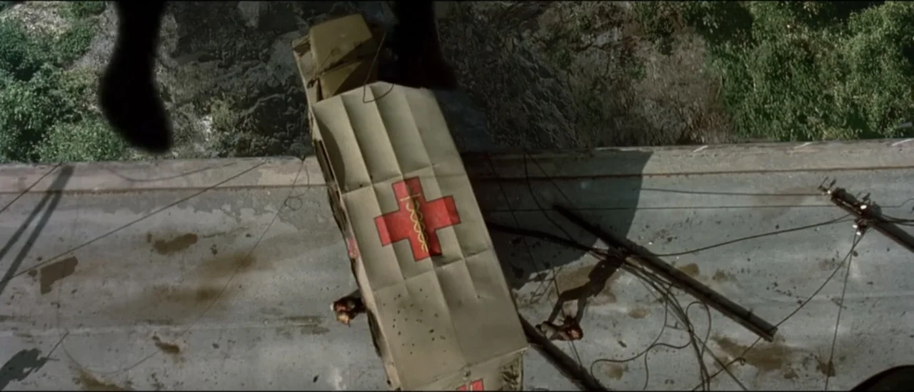 The Peacemaker (1997) movie still: wide — A damaged military-style ambulance lies on its side on a concrete bridge surface. Debris and wires scatter…