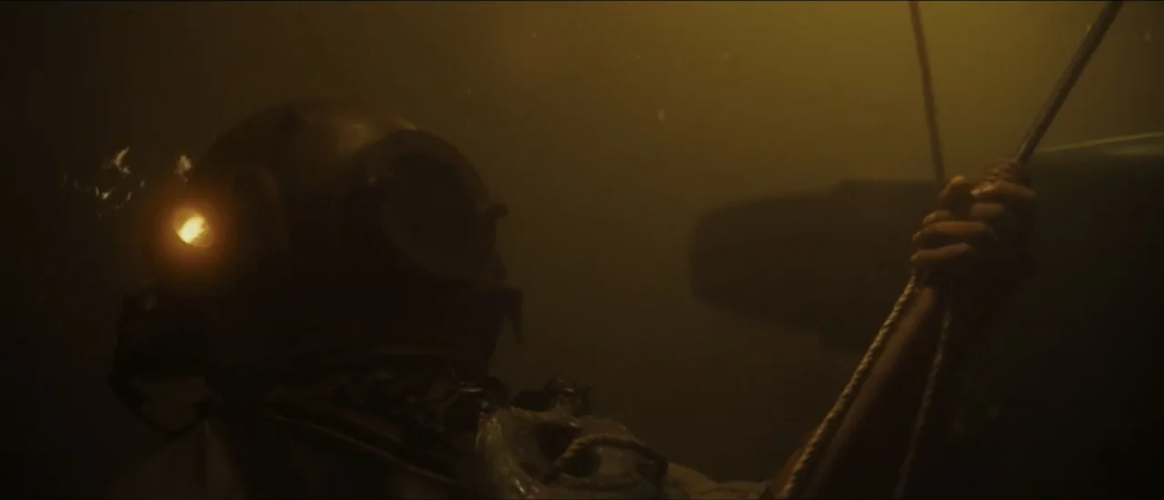 Fear Below (2025) movie still: medium — A deep underwater setting filled with murky water and low visibility. A person wearing a brass deep sea…