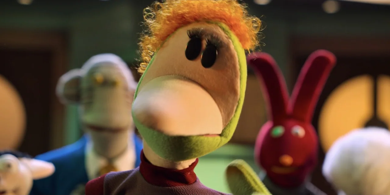 31 Minutes: One Hot Christmas (2025) movie still: closeup — A group of fabric-textured puppets stand close together in an indoor space. The central…
