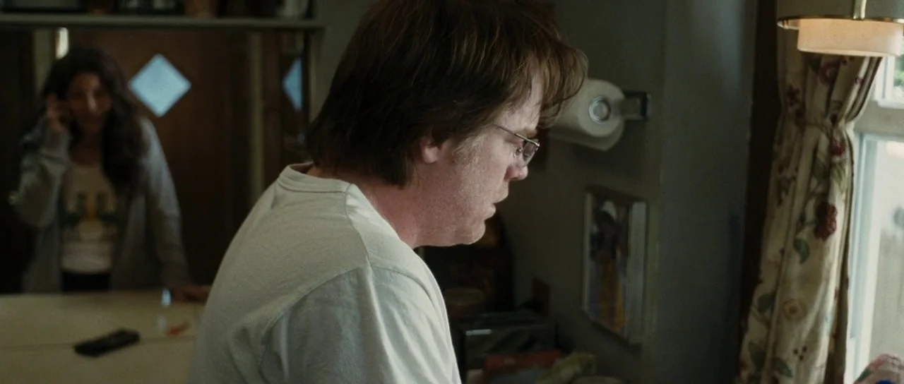 Synecdoche, New York (2008) movie still: medium — A residential kitchen features cream-colored walls, patterned floral curtains, and a paper towel…