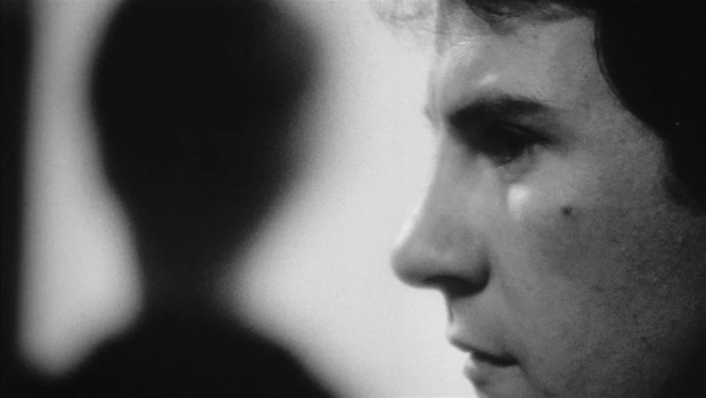 Who’s That Knocking At My Door (1967) movie still: closeup — A close-up shot focuses on a man's face in profile within a dark room. A blurred, dark…
