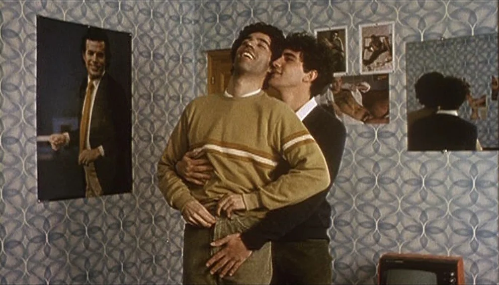 Labyrinth of Passion (1982) movie still: medium — A small room features patterned blue wallpaper covered with several framed posters and…