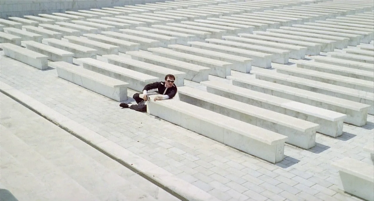 The 10th Victim (1965) movie still: wide — A vast, empty outdoor amphitheater constructed from bright white stone tiered benches. A single man in a…