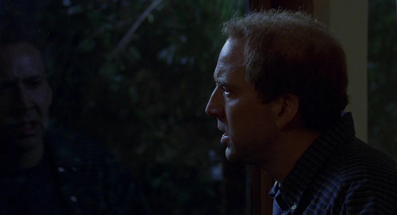 Adaptation (2002) movie still: closeup — A man looks at his reflection in a window at night. The background outside is dark with indistinguishable…