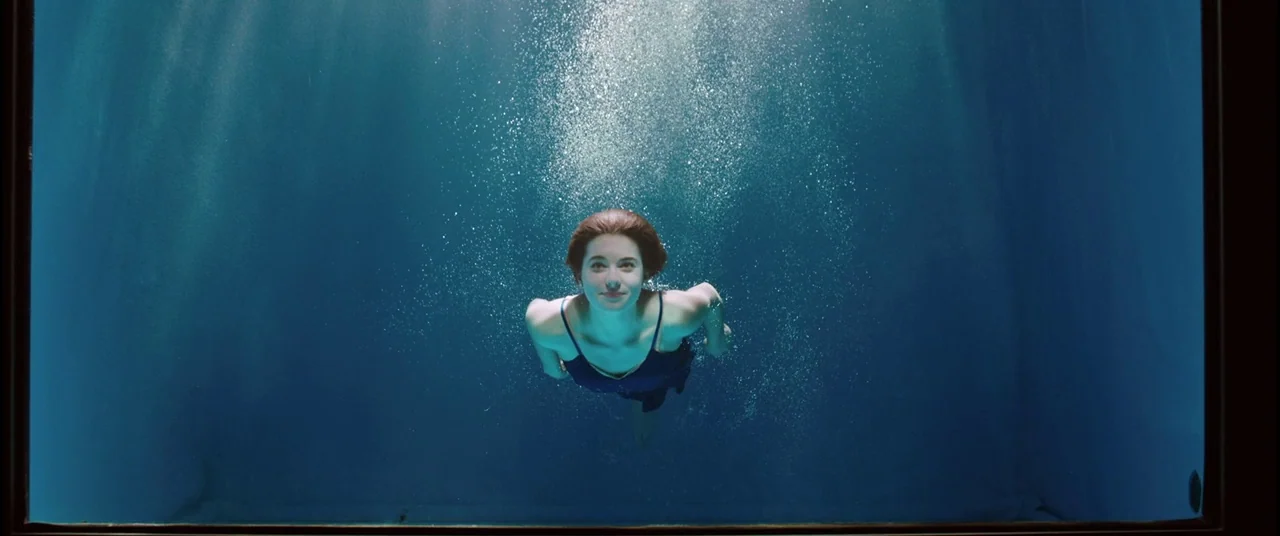 Judy (2019) movie still: medium — A woman is submerged in a deep, clear body of water. She swims toward the surface as air bubbles rise around her.