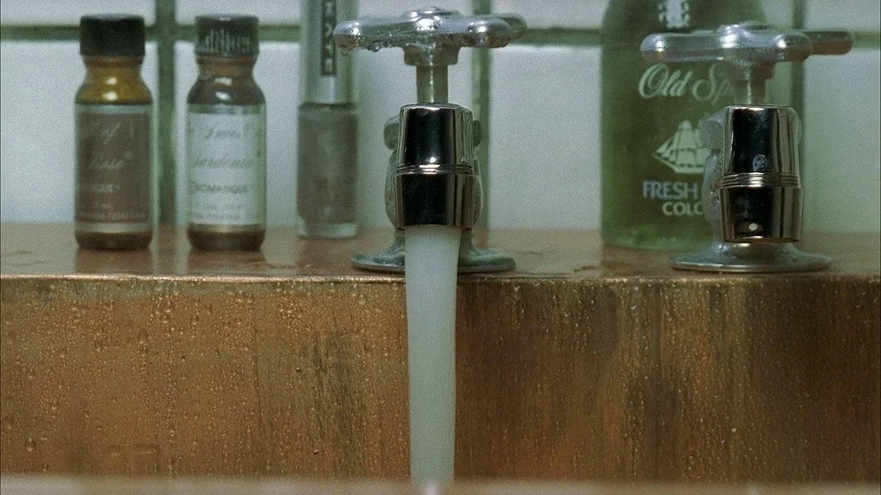 A Tale of Two Sisters (2003) movie still: closeup — A close view of a sink deck features two chrome faucets and glass bottles. A steady stream of…